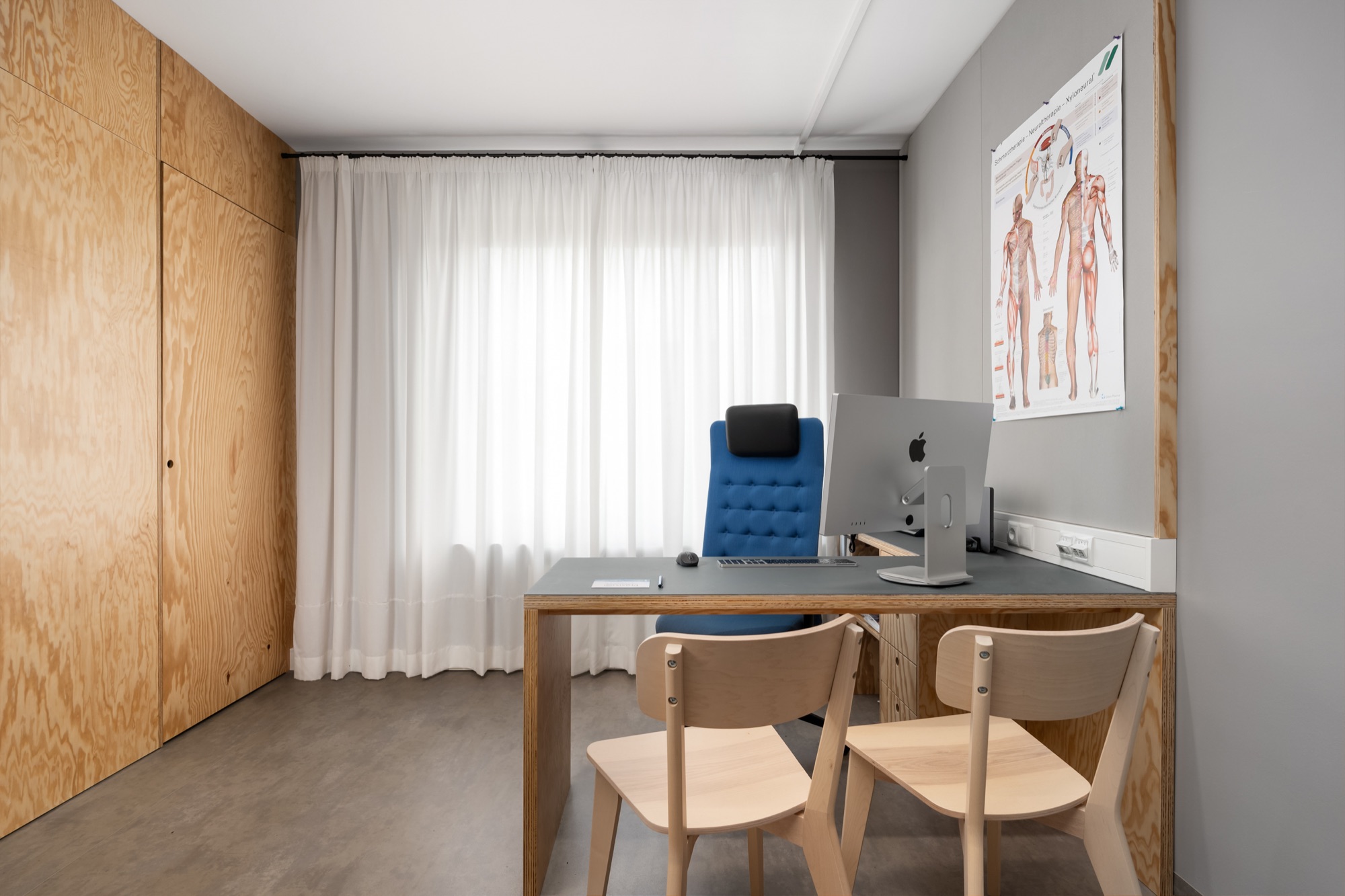Sprechzimmer der Praxis 23 mit Schreibtisch und zwei Besucherplätzen
